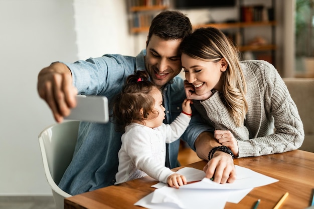 Happy parents and their small daughter taking selfie with mobile phone at home