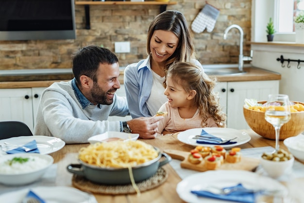 Genitori felici e la loro figlia del centro commerciale che si divertono durante il pranzo in famiglia a casa