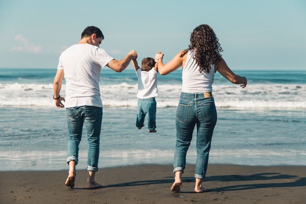 Счастливые родители бросают своего ребенка на солнечный пляж