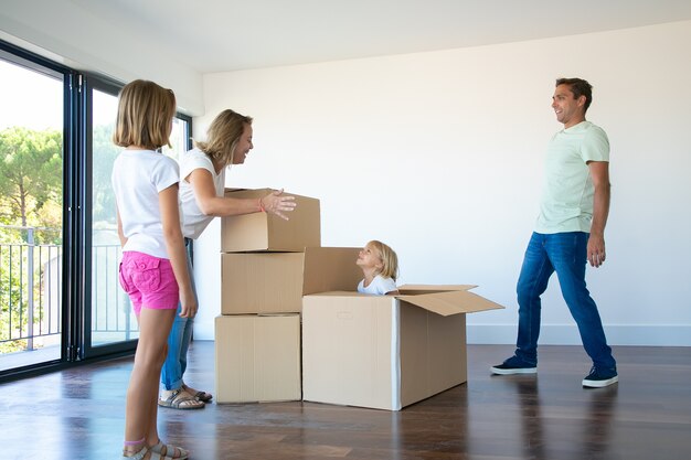 Happy parents and two daughters having fun while unpacking things in their new empty flat