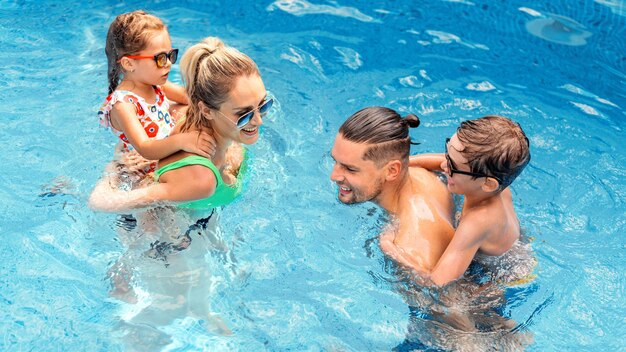 Happy parents and two kids are swimming in the pool