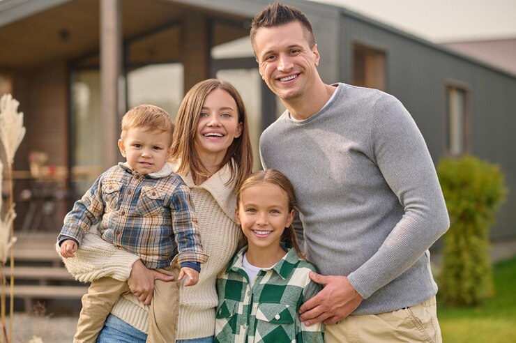 Free Photo happy people.. young beautiful woman with little boy attractive man and long-haired school-age girl in casual clothes hugging joyful looking at camera standing near house