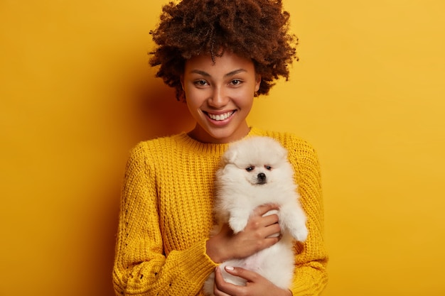 Foto gratuita felice proprietario di un animale domestico di buon umore dopo aver visitato il veterinario con il cucciolo, scopre che il suo cane spitz è sano, indossa un maglione giallo