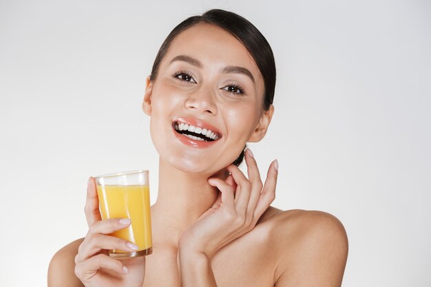반쯤 벗은 여자 웃 고 흰 벽 위에 고립 된 투명 유리에서 신선한 압착 오렌지 주스를 마시는 행복 사진