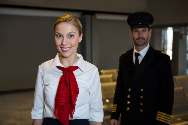 Foto gratuita felice pilota e hostess in piedi nel terminal dell'aeroporto