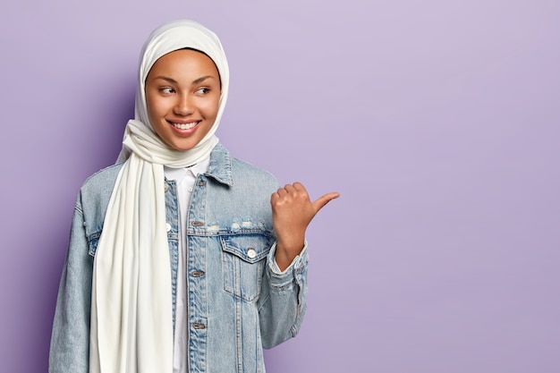 Happy pleasant looking young Muslim female shares cool promotion to you, points away