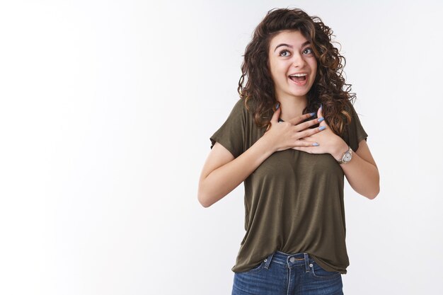 Happy pleased charming friendly girl retelling touching story press palms chest grateful thrilled smiling look up excited have lucky day grateful god, standing white background appreciating