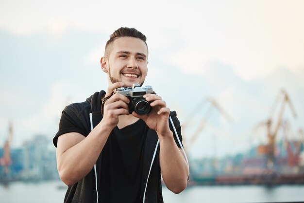 счастливый довольный фотограф широко улыбаясь, глядя в сторону и держа камеру