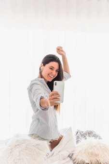 スマート​フォン​で​selfie​を​取っている​若い​女性​の​幸せな​肖像画