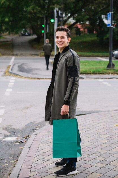 Happy portrait of smiling young man standing on sidewalk holding green shopping bag
