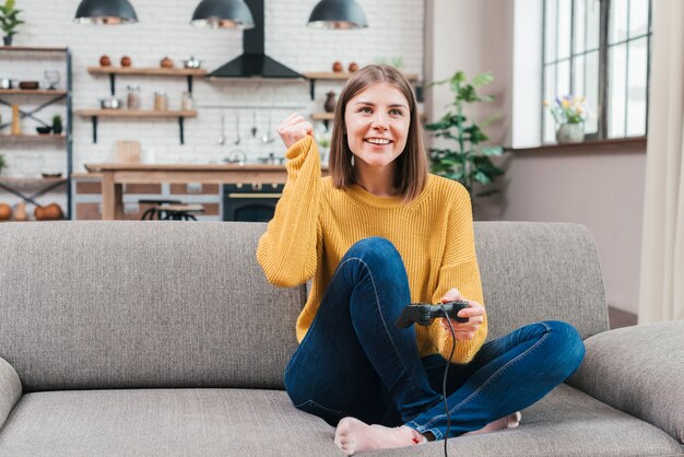 Happy portrait of a smiling young woman sitting on sofa playing the video game