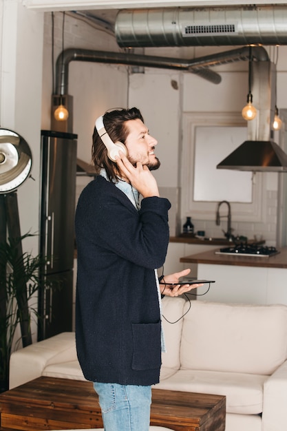 Happy portrait of a young man listening music on headphone through mobile phone at home