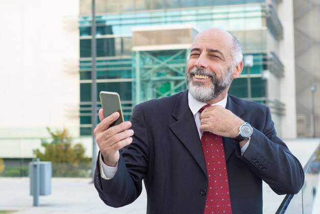 Happy positive mature business leader adjusting tie