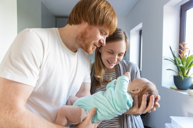 Happy positive new parents cuddling baby in arms