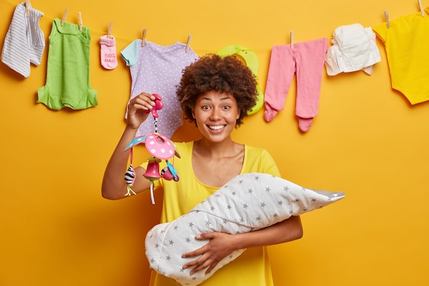 Happy positive woman carries baby in blanket holds mobile gives new life for daughter dressed in casual dress poses 