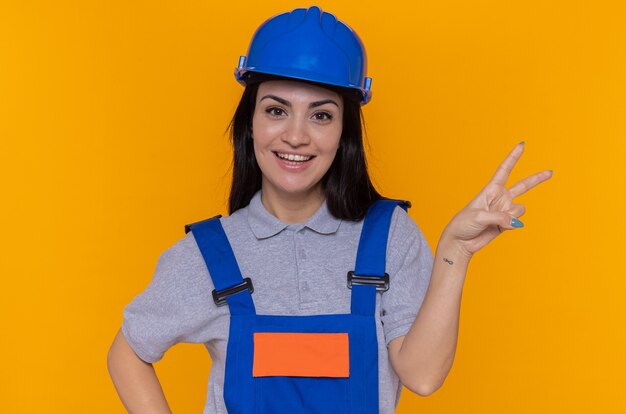 Happy and positive young builder woman in construction uniform and safety helmet