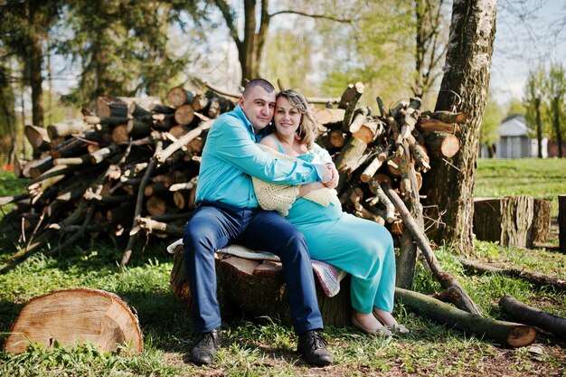 Happy pregnant family dressed in a turquoise clothes sitting on a stump at park