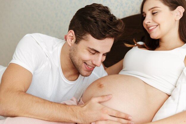 Счастливая беременная жена лежит в постели со своим мужем