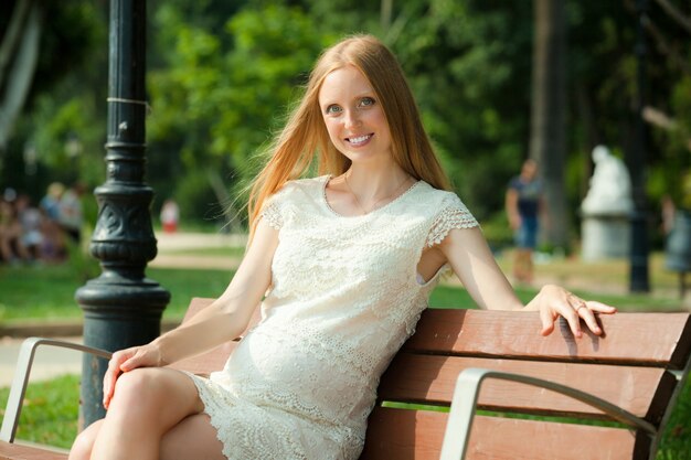 happy pregnant woman on a bench in the park in summer