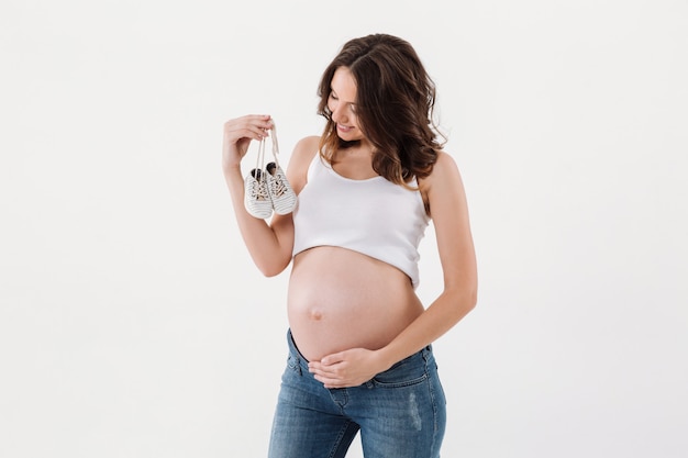 Happy pregnant woman holding little baby shoes.