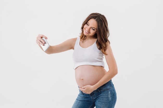 Счастливая беременная женщина делает селфи с ее животом