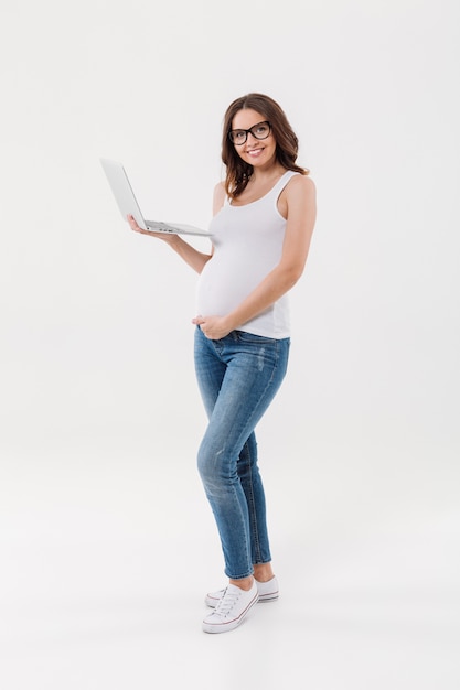 Happy pregnant woman wearing glasses using laptop