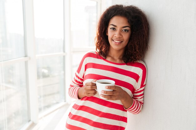 happy pretty african woman drinking coffee near the window