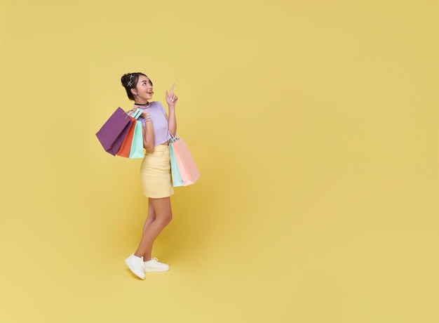 Free photo happy pretty asian woman carrying colorful shopping bags looking and pointing finger