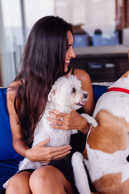 Счастливая довольно красивая женщина отдыхает дома на диване с домашними собаками