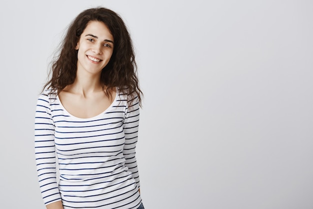 Happy pretty girl smiling broadly, standing grey wall