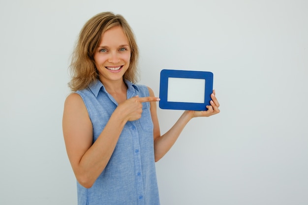 Free photo happy pretty lady pointing at empty picture frame