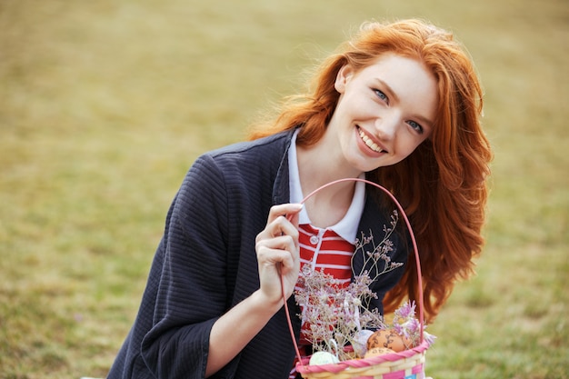 Счастливая милая женщина держа корзину для пикника с пасхальными яйцами outdoors
