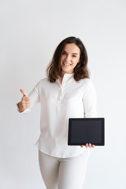 Happy pretty woman holding tablet computer, showing its screen, looking at camera 