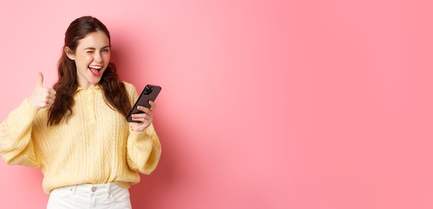 Free photo happy pretty woman saying yes holding mobile phone and making thumbs up gesture approve good thing s
