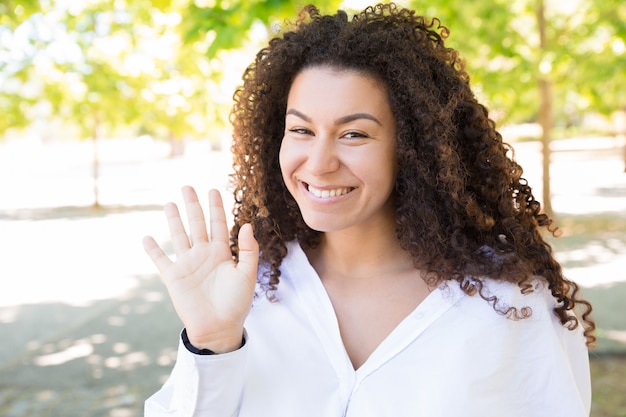 Free photo happy pretty young lady waving hand to you in park