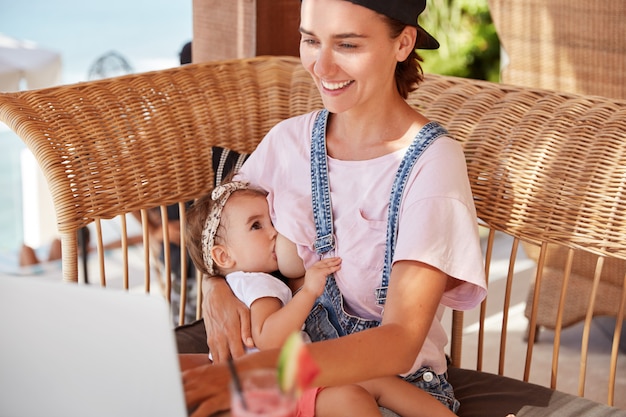 幸せなかなり若い母親が小さな子供を母乳で育てる、インターネットで母親のブログを読む、小さな子供たちの世話をする方法のアドバイスを受け取る