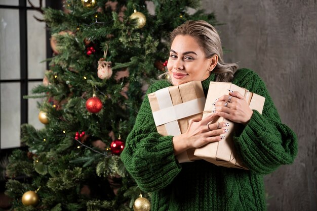 クリスマスツリーの近くにギフトボックスを抱き締めて幸せなかなり若い女性