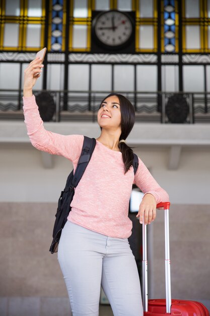 Happy pretty young woman taking selfie photo in station hall