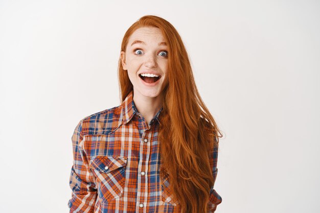 Free photo happy redhead girl student looking happy and surprised at front, receiving present, standing over white wall