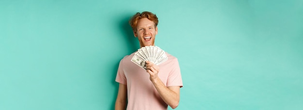 Free photo happy redhead man in tshirt showing money in dollars and smiling making smug faces after winning cas