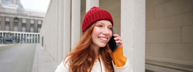 無料写真 電話で話している幸せな赤毛の女性の女の子は、インターネットを使用して電話をかけるモバイルアプリで会話をしています
