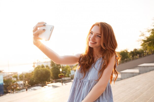 Selfieを取って長い髪の幸せな赤毛の女性