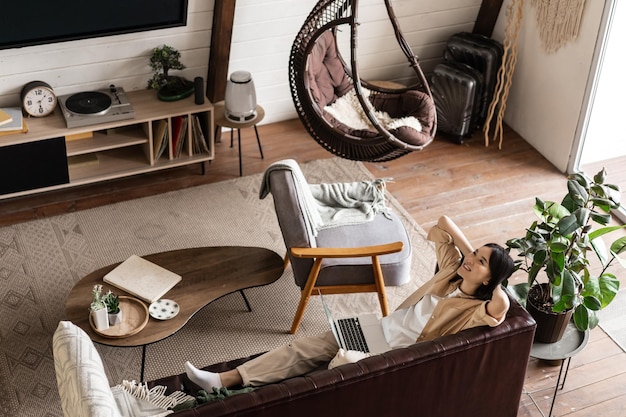 Free photo happy relaxed asian woman laying on couch at home with laptop listening podcast and enjoying weekend