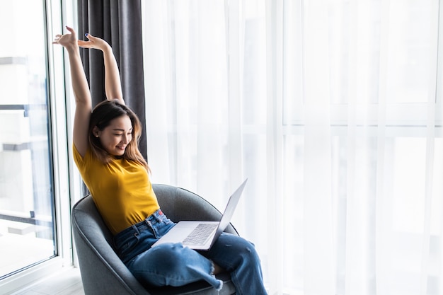 Free photo happy relaxed casual woman sitting on the chair with a laptop in front of her stretching her arms above her head