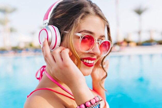 Happy relaxing girl looking to camera through pink sunglasses and pretty smiling on exotic background