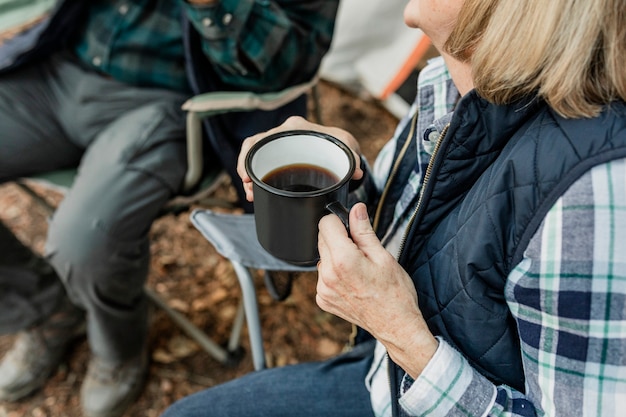 Happy retired couple having coffee by the tent in the forest