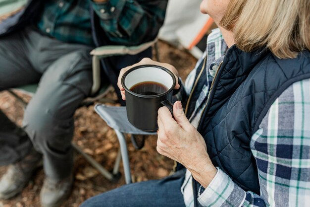 Счастливая пара пенсионеров, пьющих кофе у палатки в лесу