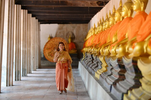 伝統的なタイのドレスで幸せな引退した女性は、寺院で旅行します。