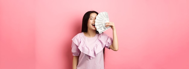 무료 사진 행복 한 부자 아시아 여자 돈을 보여주는 핑크 b에 대 한 드레스에 서 있는 현금으로 쇼핑 웃 고