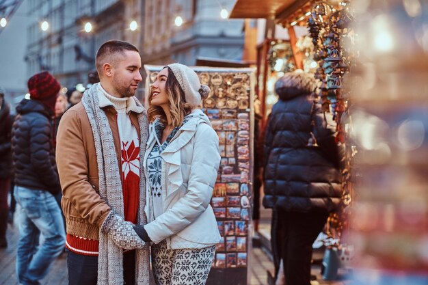 a happy romantic couple holding hands while standing on the street at christmas time